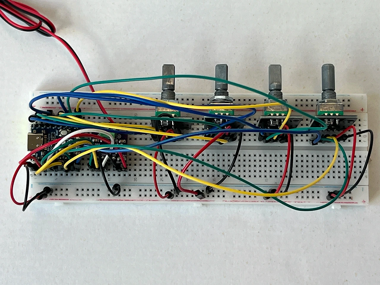 Das fertige Gerät von oben: Die vier Regler stehen mit ihren Metallachsen in einer Reihe am oberen Rand des Steckbretts, links davon sitzen Chip und Audioboard. Blaue, grüne, gelbe, rote und schwarze Kabel spannen sich kreuz und quer darüber; oben links laufen zwei Adern aus dem Bild zum Lautsprecher.